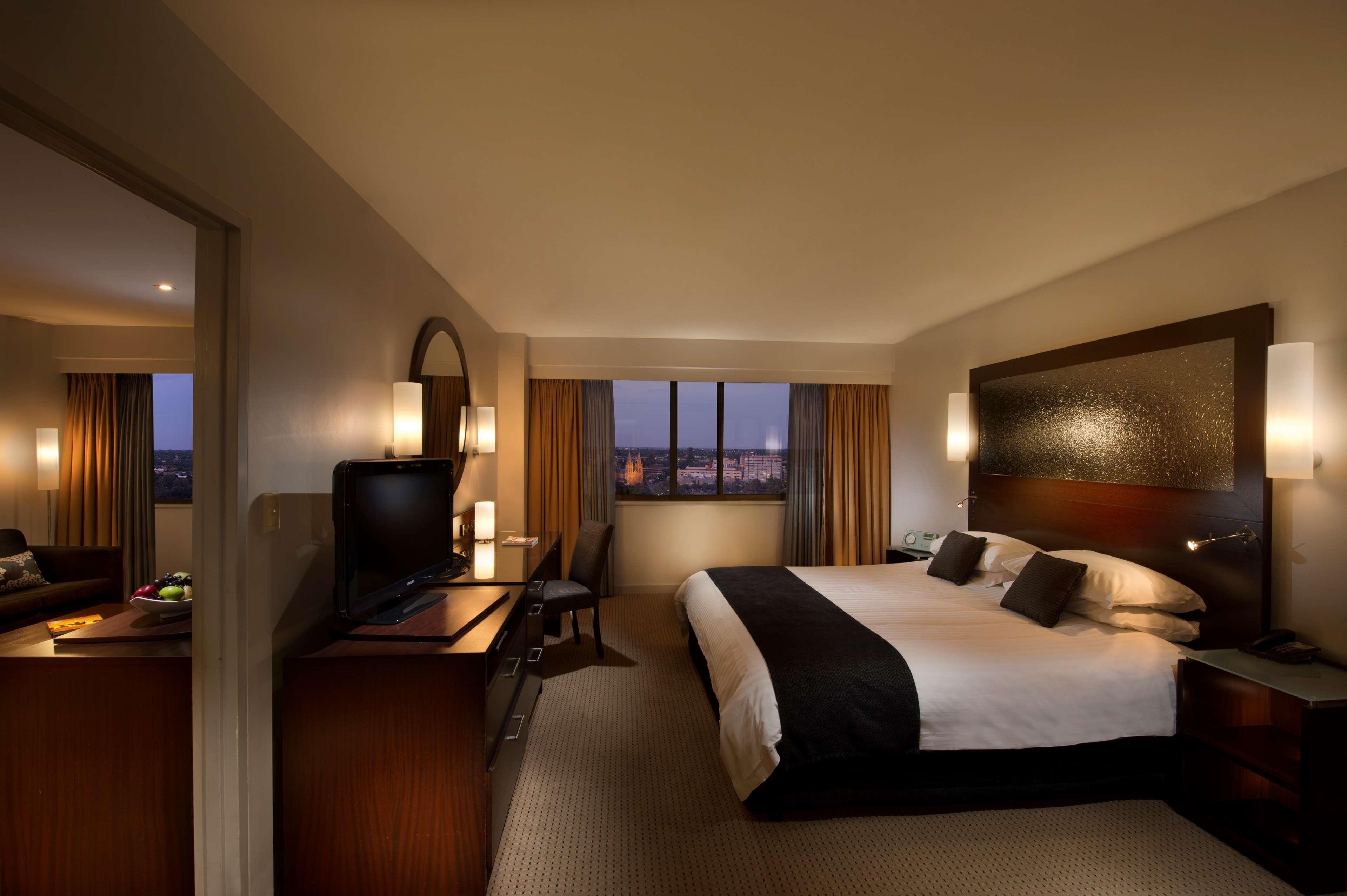 斯坦福德阿德莱德广场酒店 外观 照片 The photo features a modern hotel room that includes a large bed with dark and light bedding, complemented by two pillows. The room is well-lit with warm lighting and has a contemporary aesthetic. To one side, there is a wooden dresser with a flat-sc