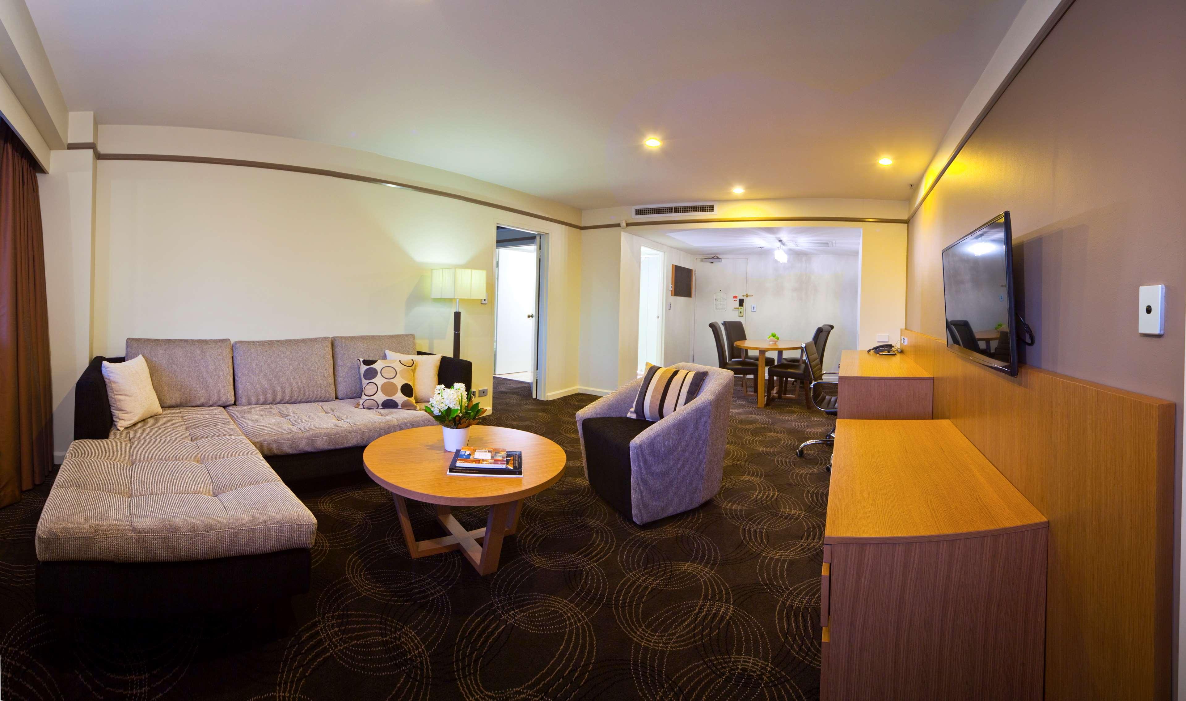 斯坦福德阿德莱德广场酒店 外观 照片 The photo shows a spacious living area with modern decor. On the left, there is a light gray sectional sofa, accompanied by a round wooden coffee table in front of it. A couple of decorative pillows add a touch of color to the sofa. To the right, the