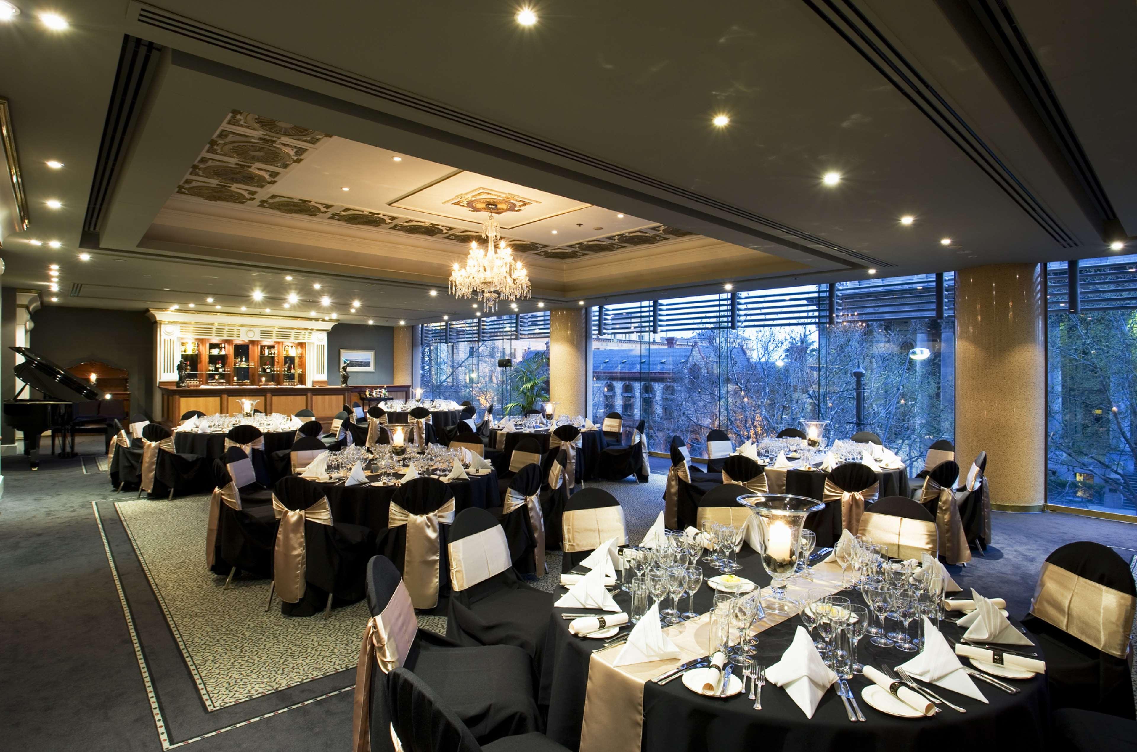 斯坦福德阿德莱德广场酒店 外观 照片 The photo shows an elegant banquet hall or restaurant setting. There are several round tables covered with black tablecloths and adorned with gold accents. Each table is set with fine dining utensils, glassware, and neatly folded napkins. In the back