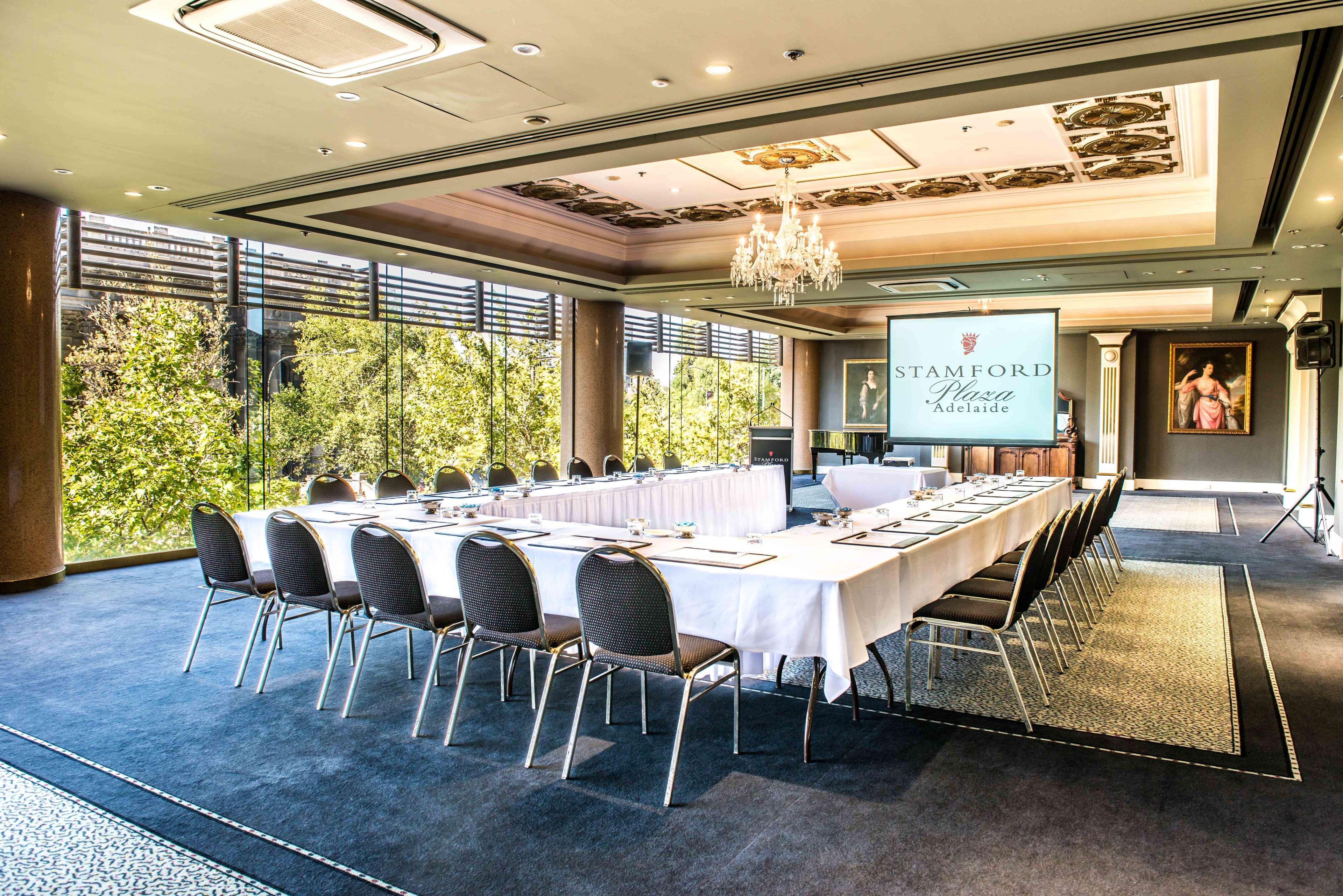 斯坦福德阿德莱德广场酒店 外观 照片 The photo shows a stylish conference room set up for a meeting or event. There is a long rectangular table covered with a white tablecloth, surrounded by black chairs. A large screen displays the name "Stamford" along with a logo. The room features l