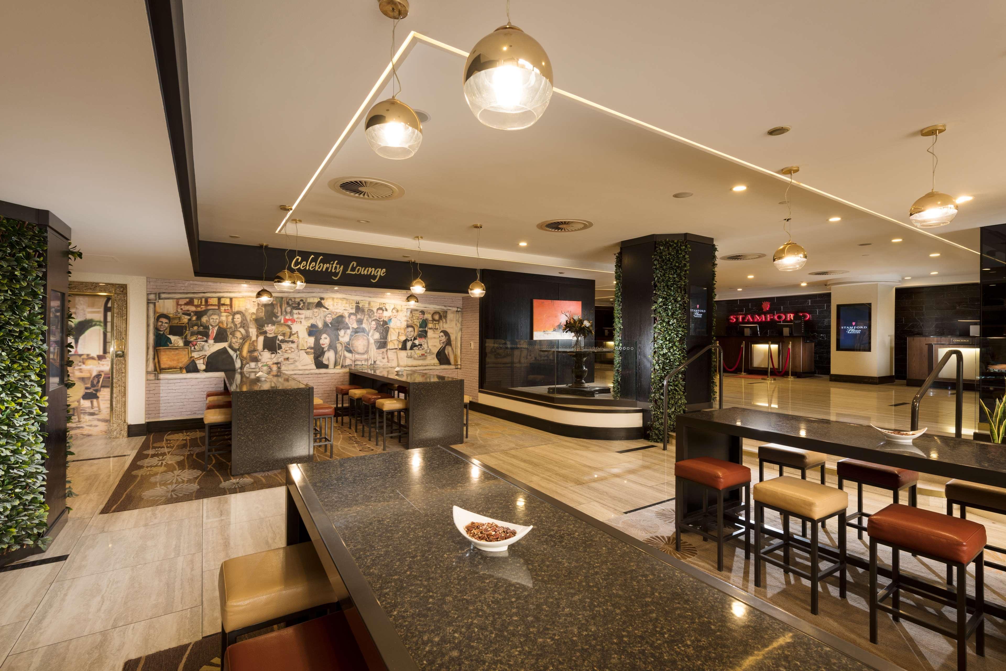 斯坦福德阿德莱德广场酒店 外观 照片 The photo shows a modern and stylish interior of a lounge or restaurant area. Prominent features include a long dark countertop with bar stools, and several pendant lights hanging from the ceiling. In the background, there is a mural or artwork that 